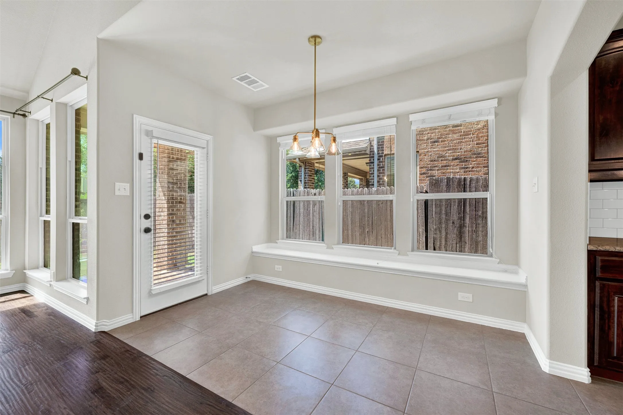 Tile flooring, multiple windows, window bench, pendant light fixture, and a glass-paneled door