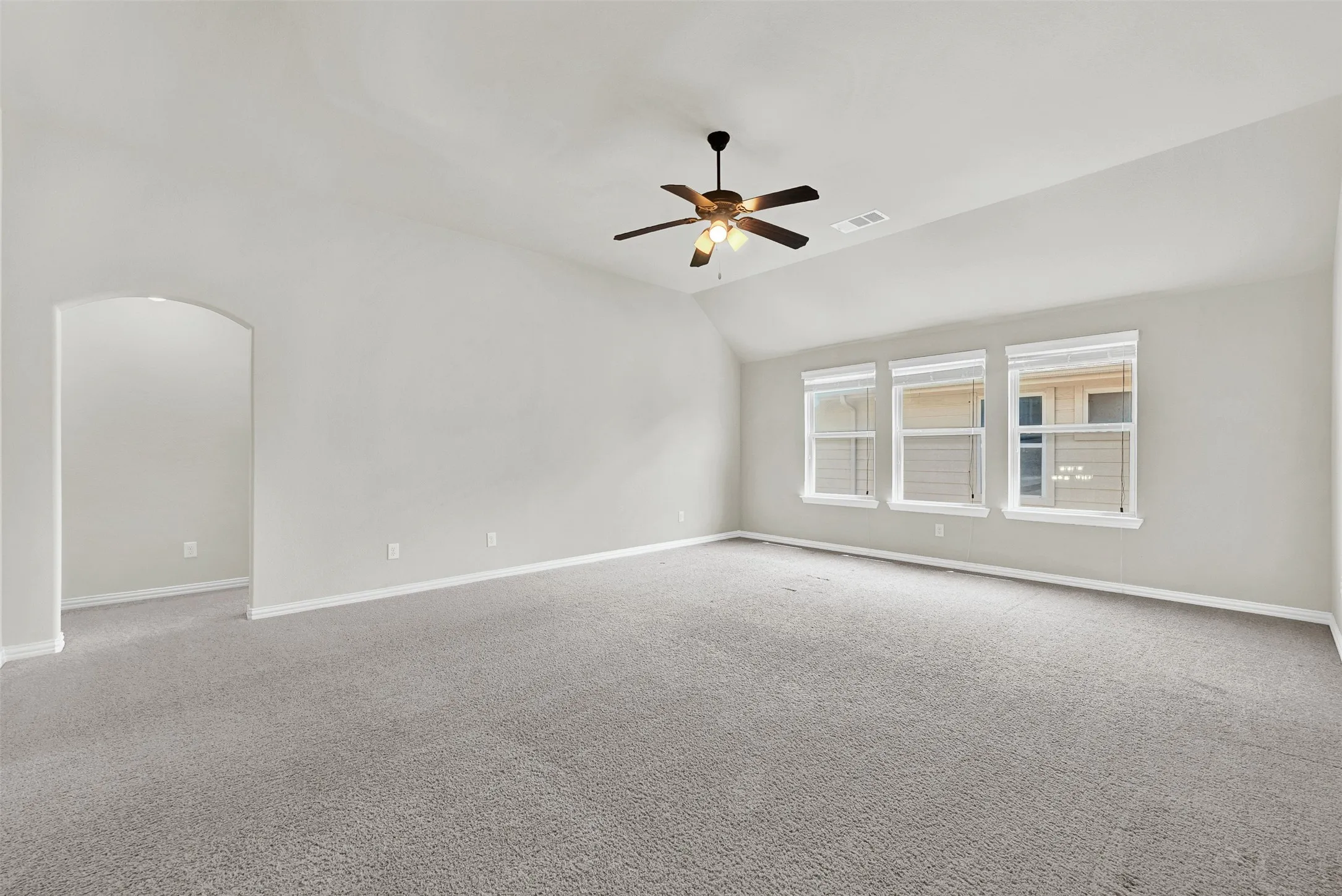 Spacious room featuring vaulted ceilings, light gray carpeting, a multi-light ceiling fan, and three large windows