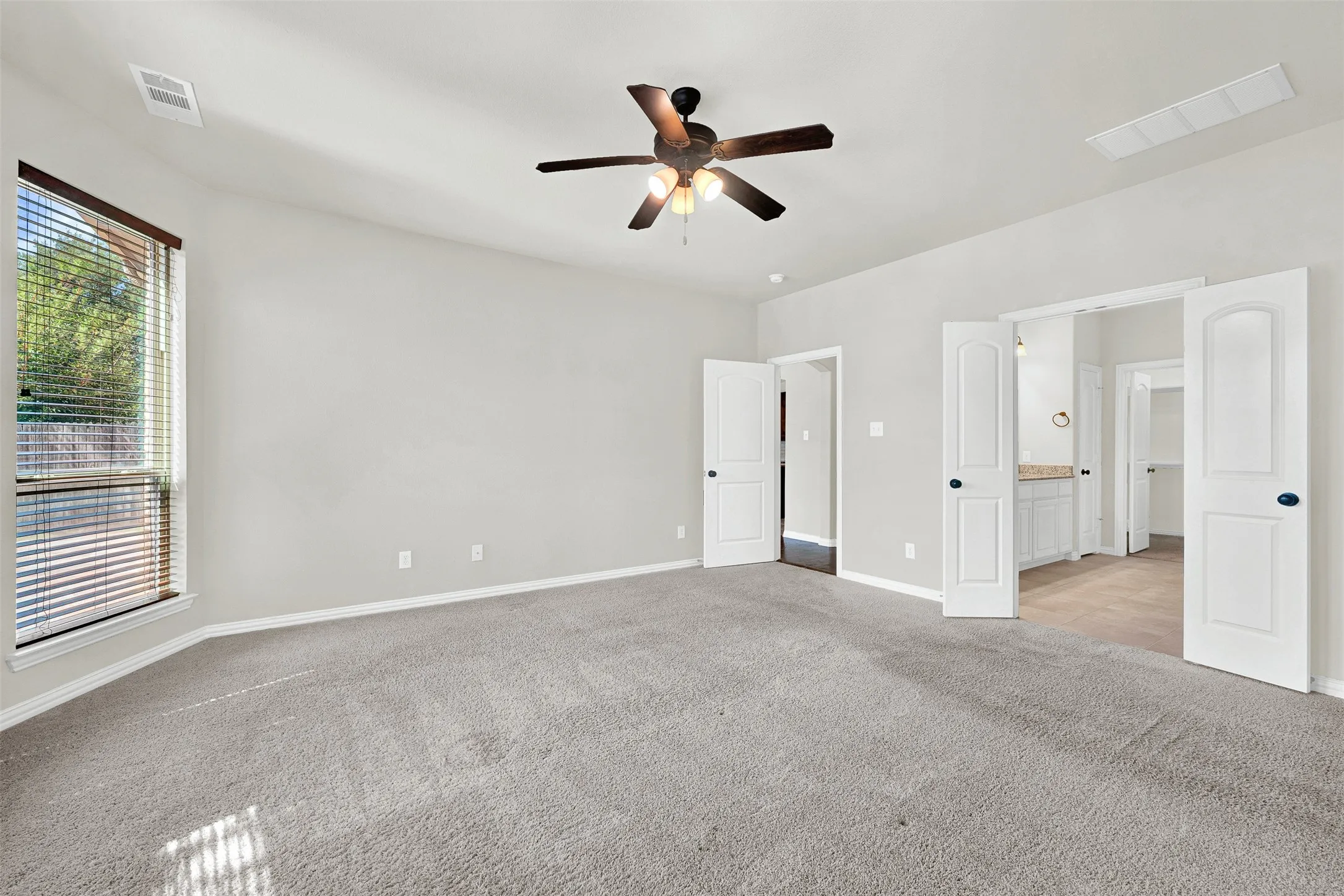 Spacious room featuring carpeting, a ceiling fan with integrated lighting, and multiple paneled doors