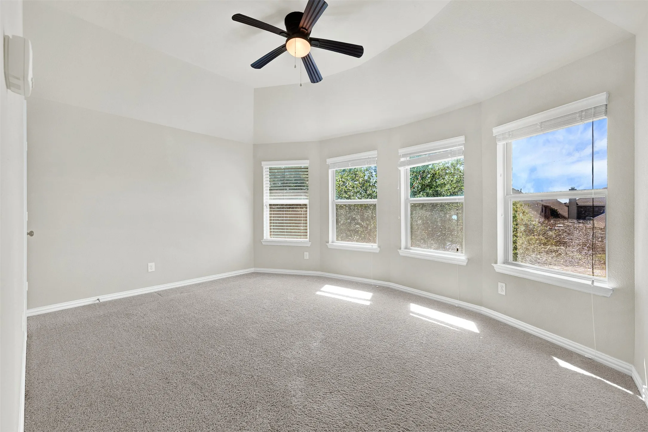 Vaulted ceiling, ceiling fan, gray carpeting, multiple windows, and light gray wall paint