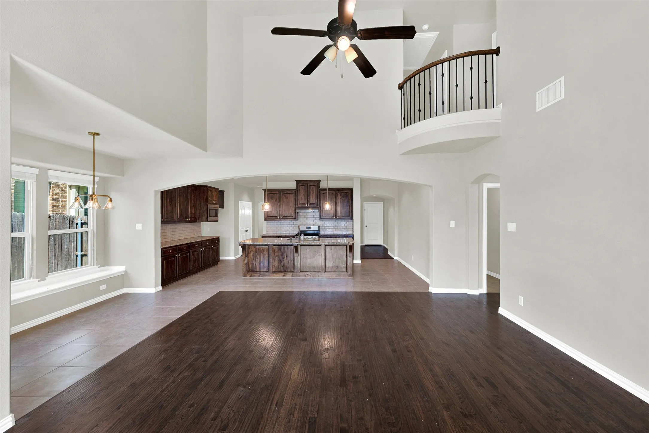 Two-story living area with dark wood-finish flooring, a ceiling fan, and a second-story balcony with metal balusters