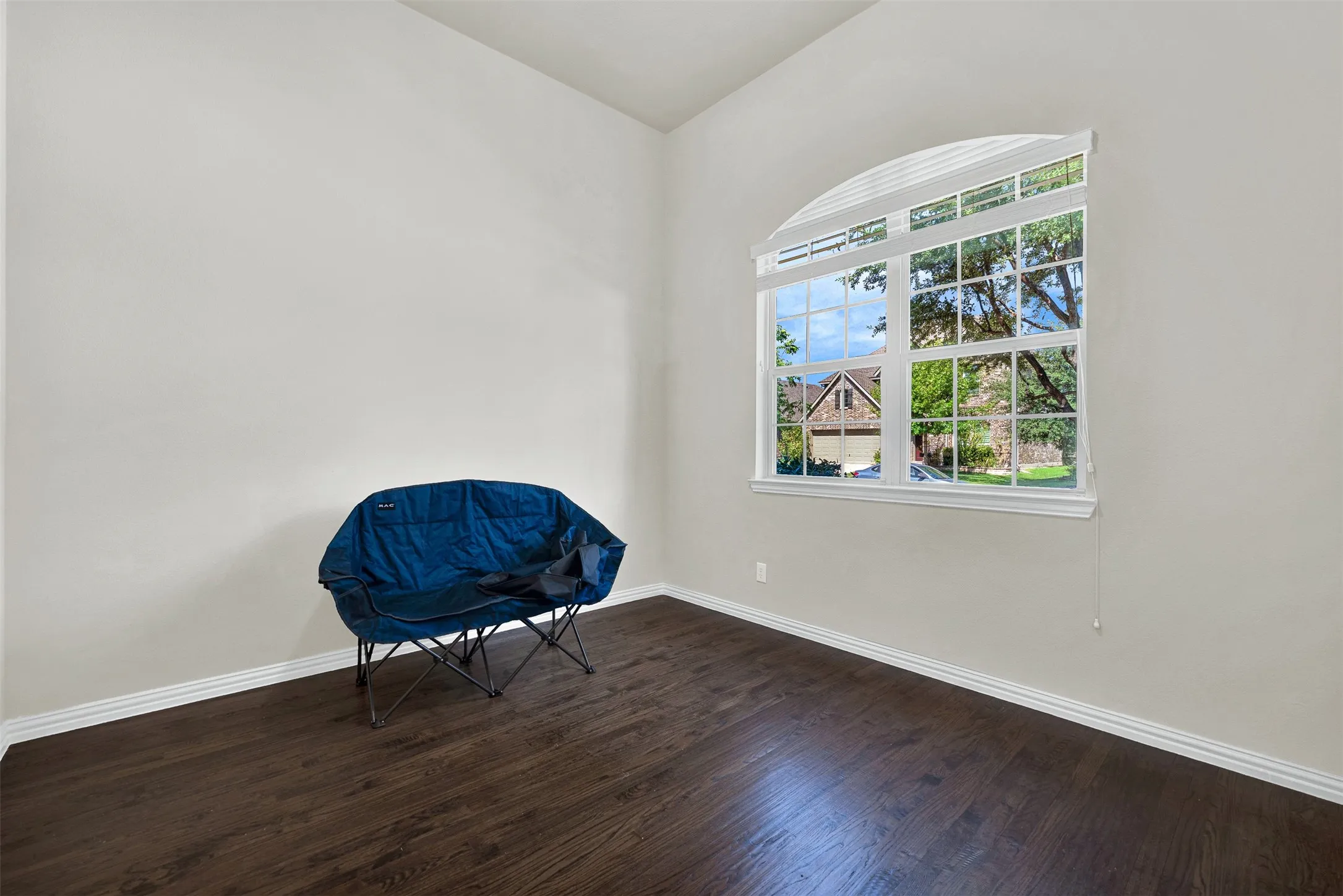 Arched window with blinds, wood-finish flooring, and white baseboards