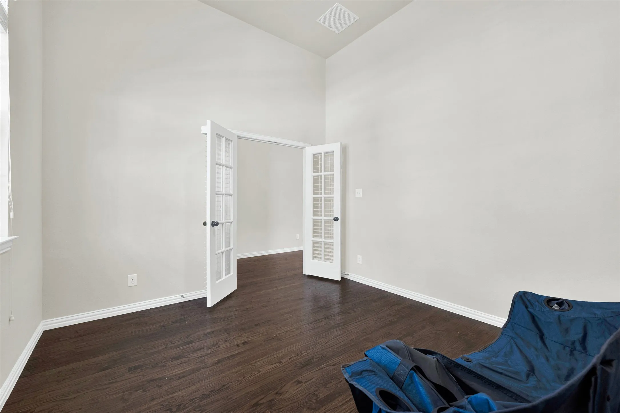 Vaulted ceiling, wood-finish flooring, white walls, and double French doors with louvered panels