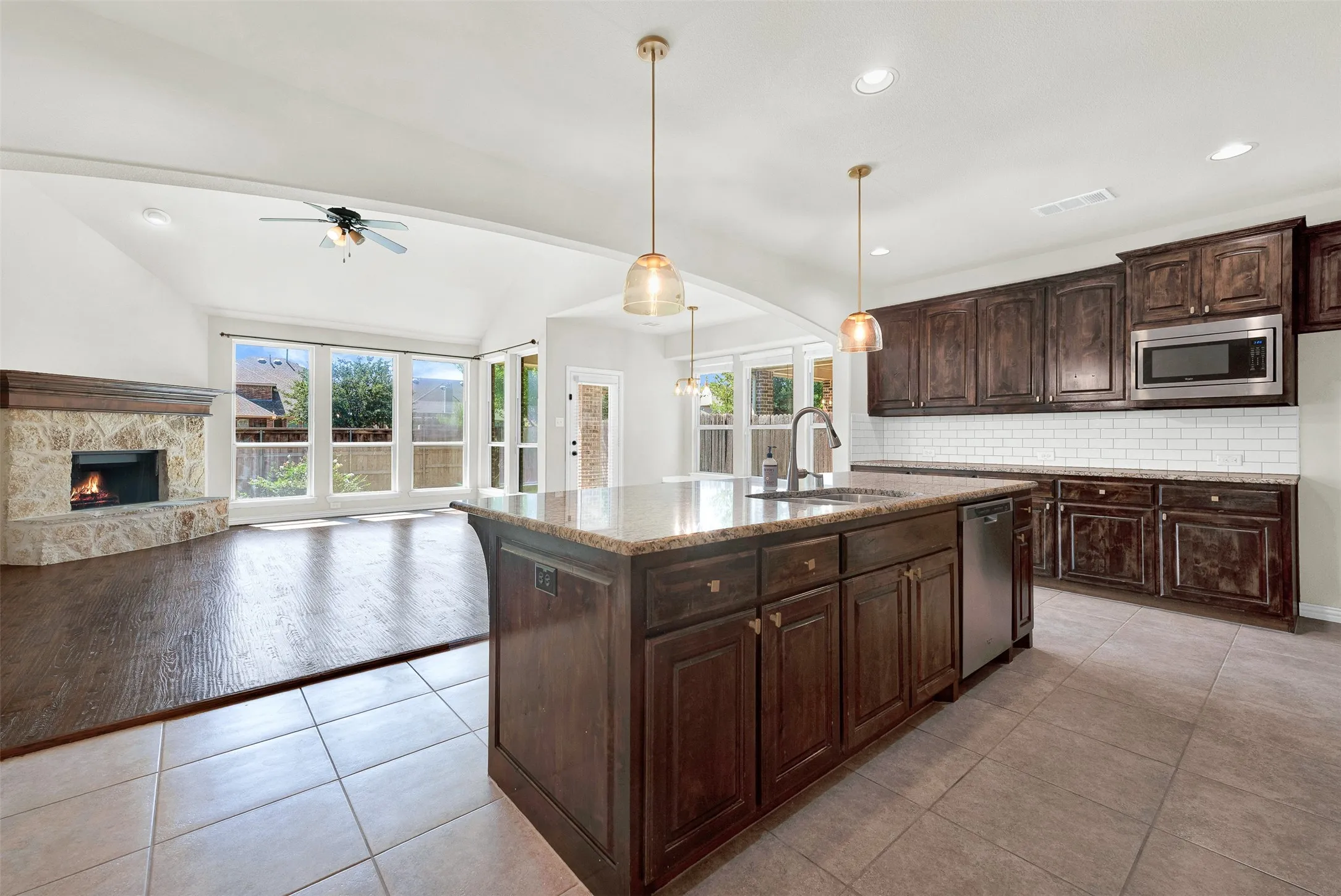 Open-concept design featuring a central kitchen island with a built-in sink, dark wood-finish cabinetry, and stainless steel appliances