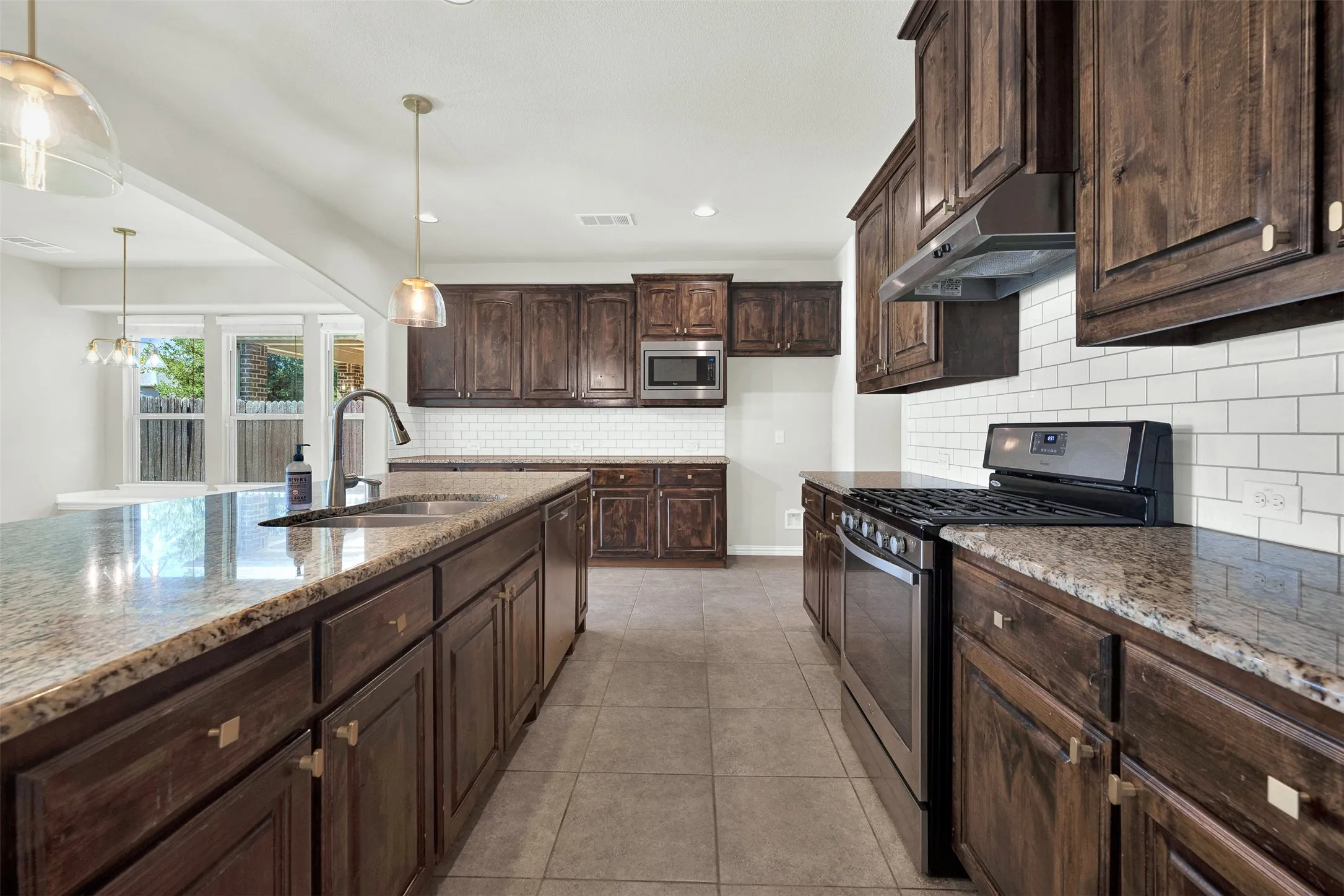 Kitchen featuring stone countertops, dark wood-finish cabinetry, a subway tile backsplash, stainless steel appliances, and tile flooring