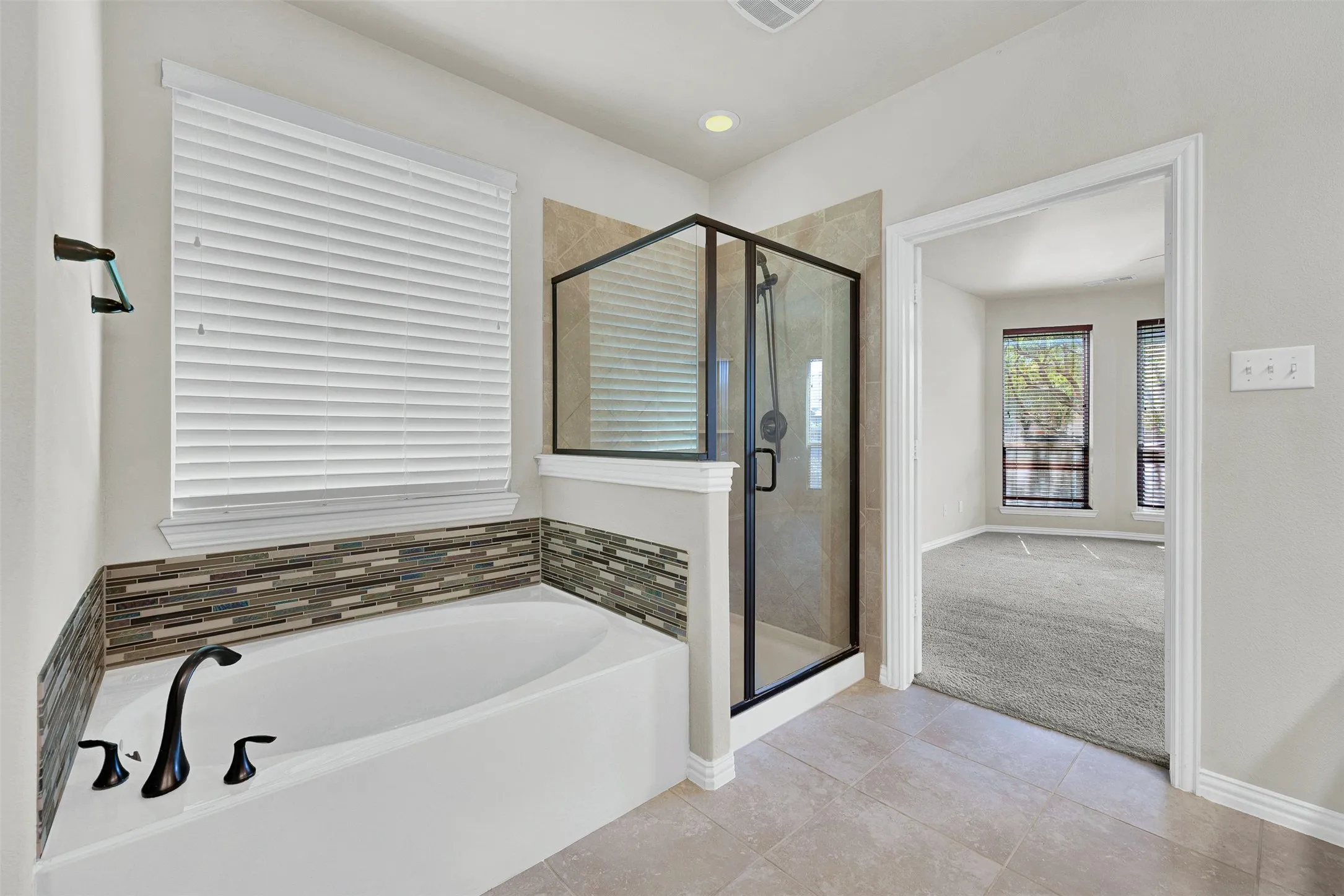 Soaking tub with mosaic tile surround, enclosed glass shower, matte black fixtures, and ceramic tile flooring