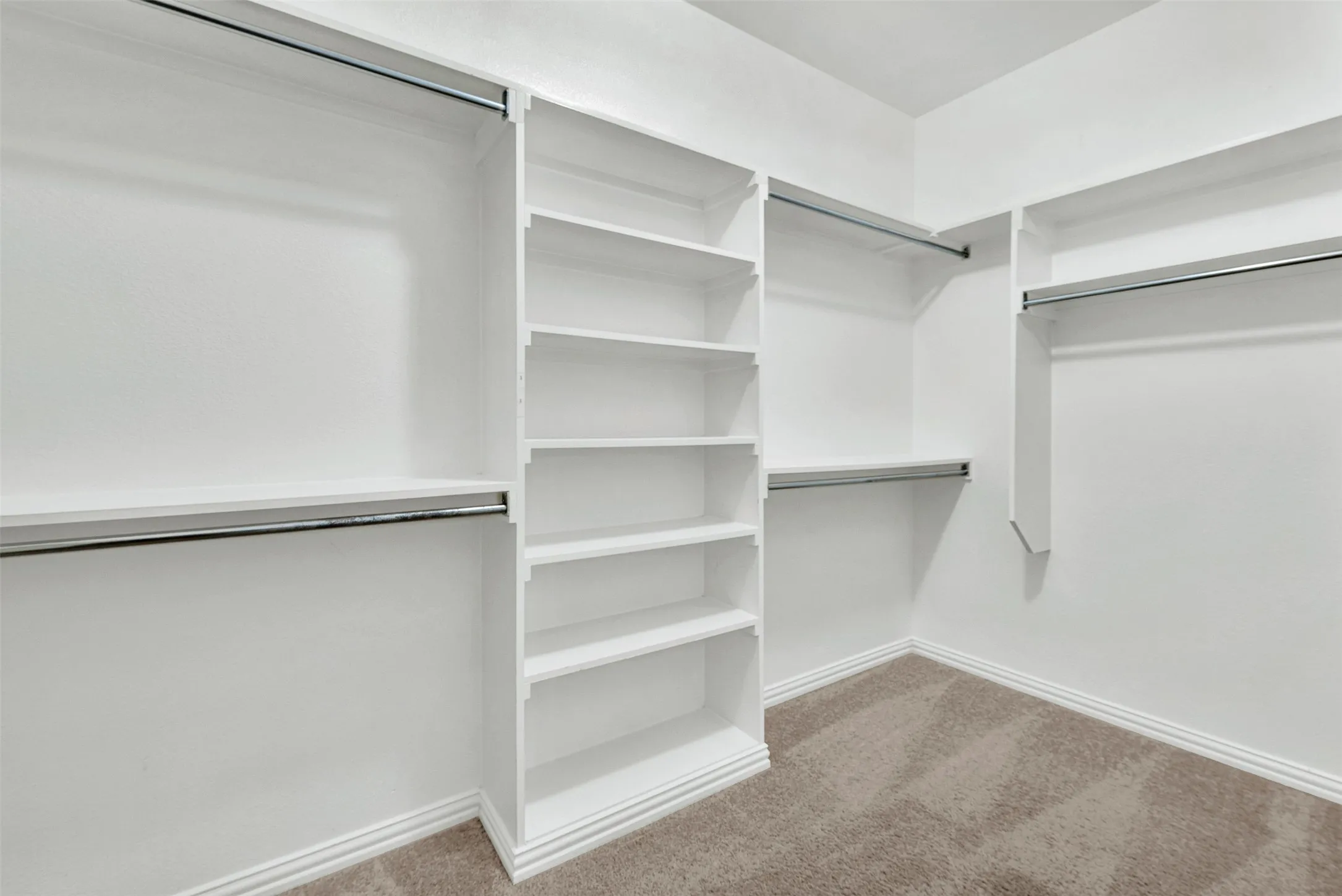 Walk-in closet featuring built-in shelving, multiple hanging rods, and carpet flooring