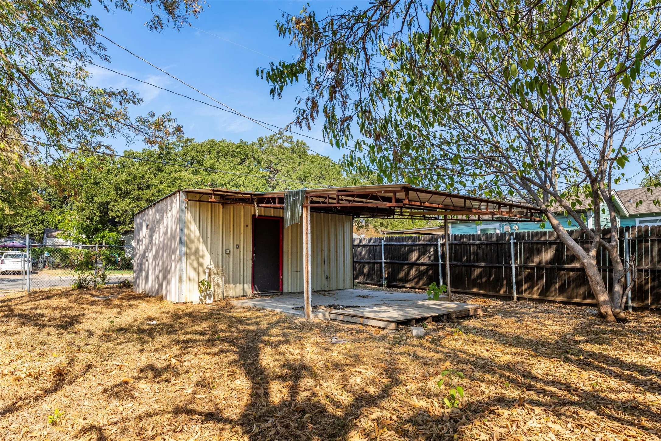 Corrugated metal structure with an attached metal-frame awning, concrete patio, and partially fenced yard