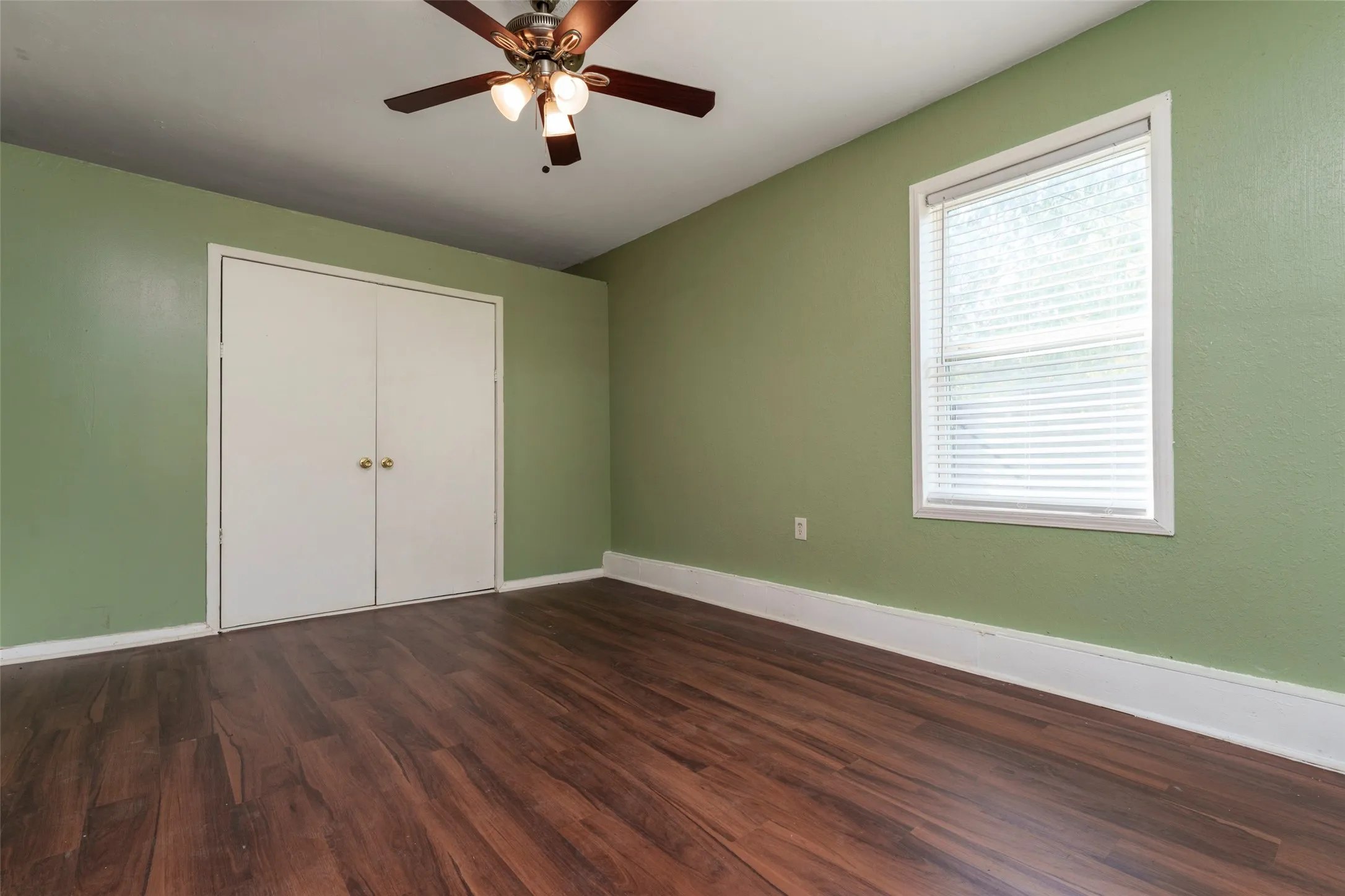 Wood-finish flooring, white bi-fold closet doors, and a ceiling fan with integrated lighting
