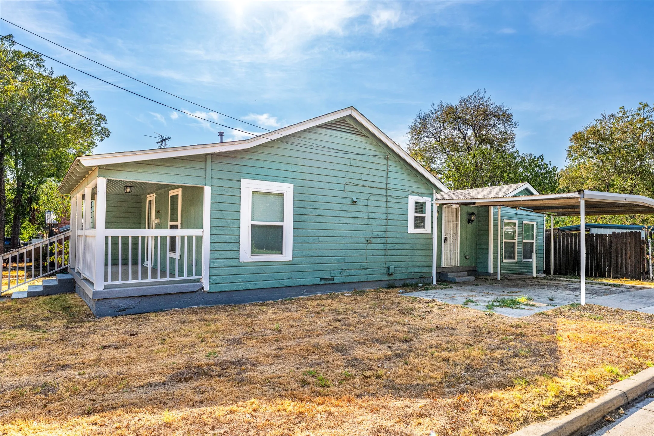 Siding exterior featuring a covered porch with white railing, covered carport, and a separate structure