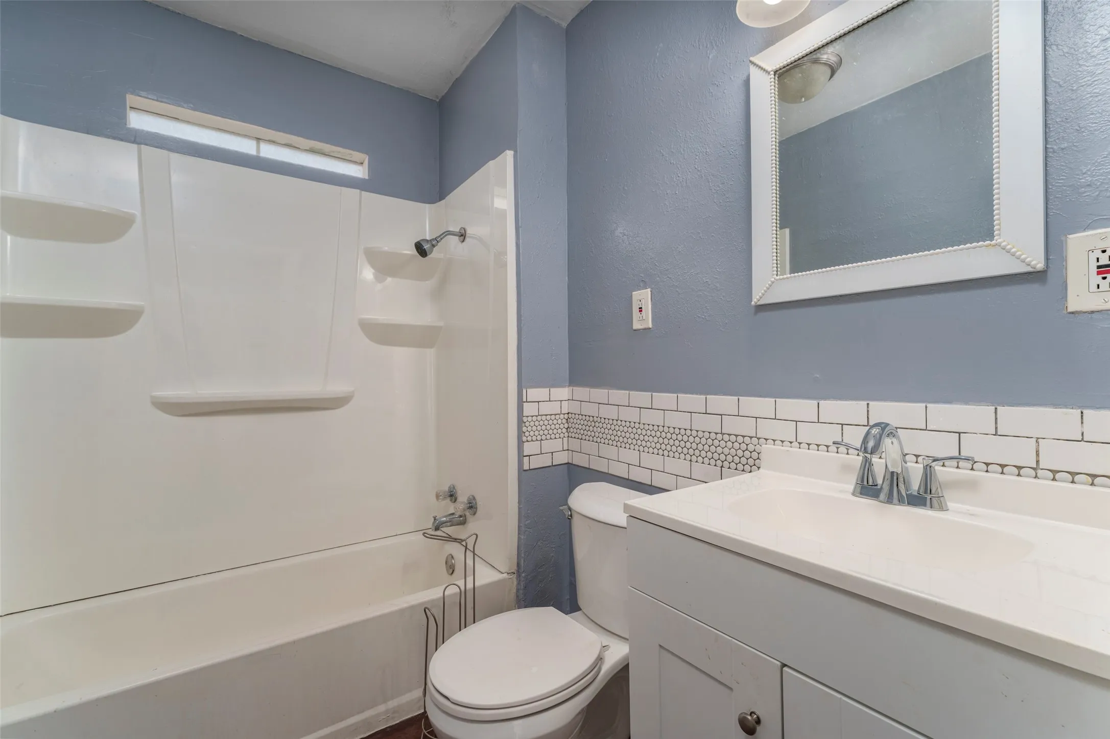 White subway tile wainscoting with a mosaic accent band, white vanity with integrated sink, chrome faucet, and white framed mirror