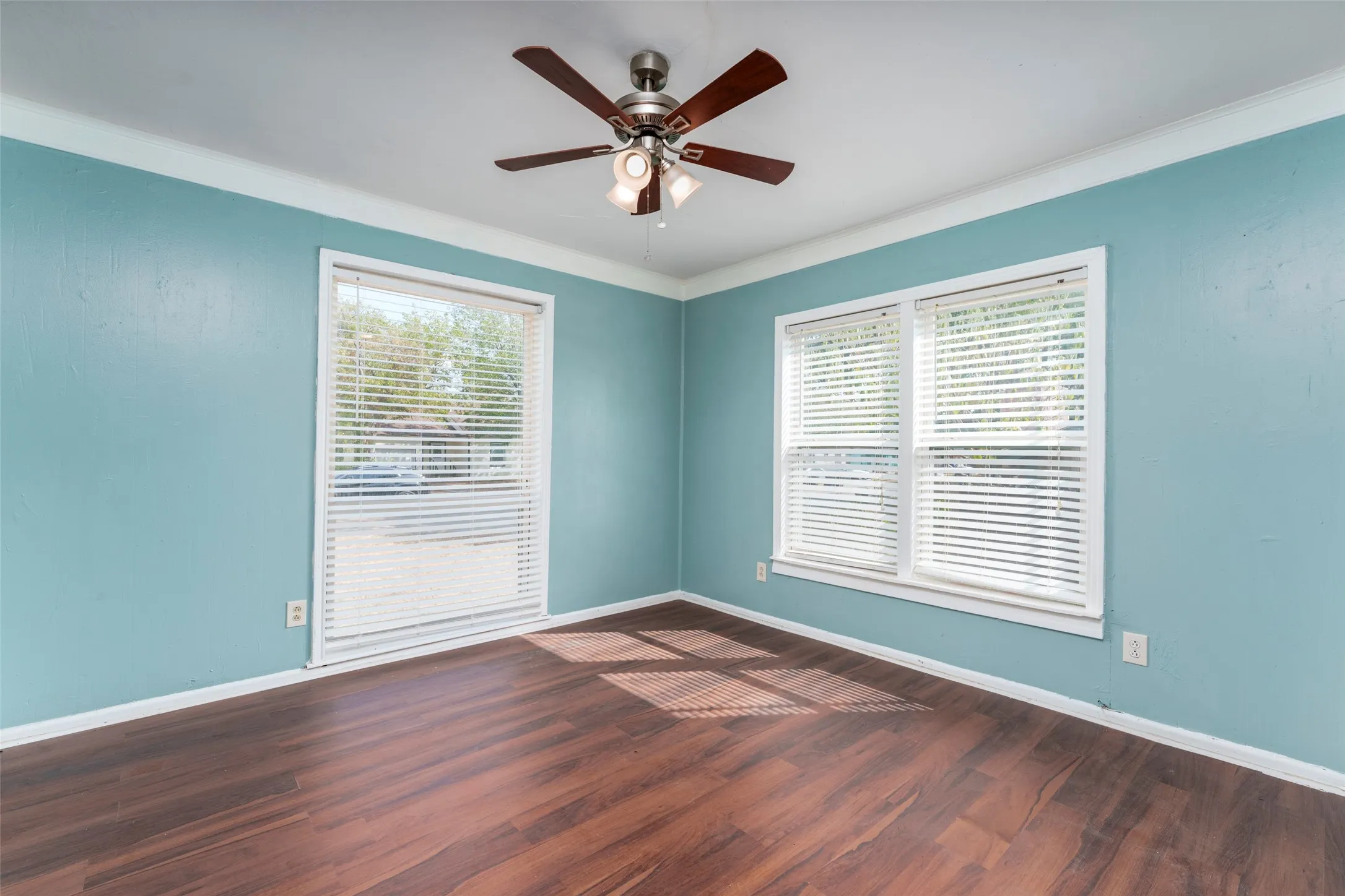 Wood-finish flooring with two windows, a ceiling fan, and white trim