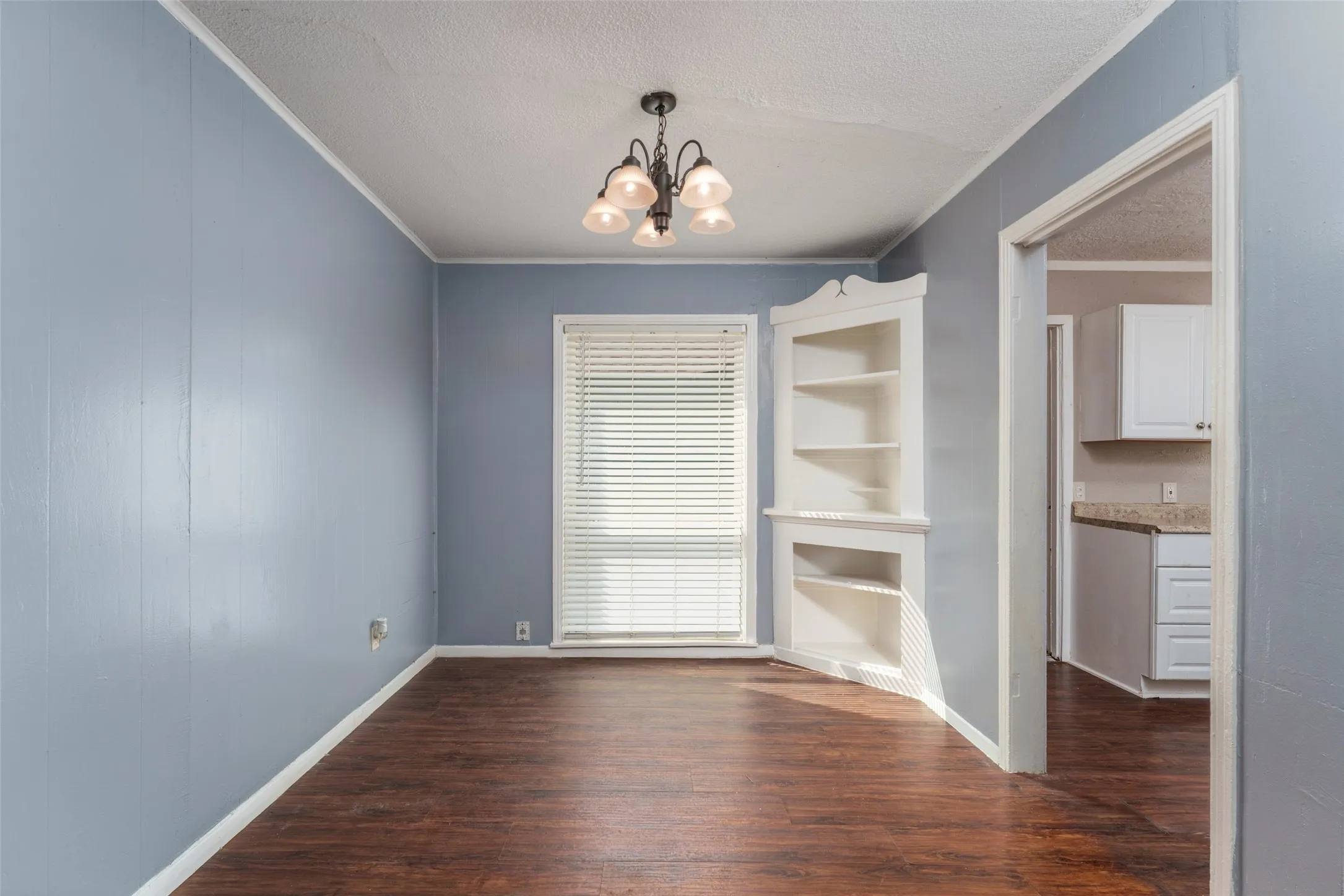 Wood-finish flooring with a multi-light chandelier and corner built-in shelving