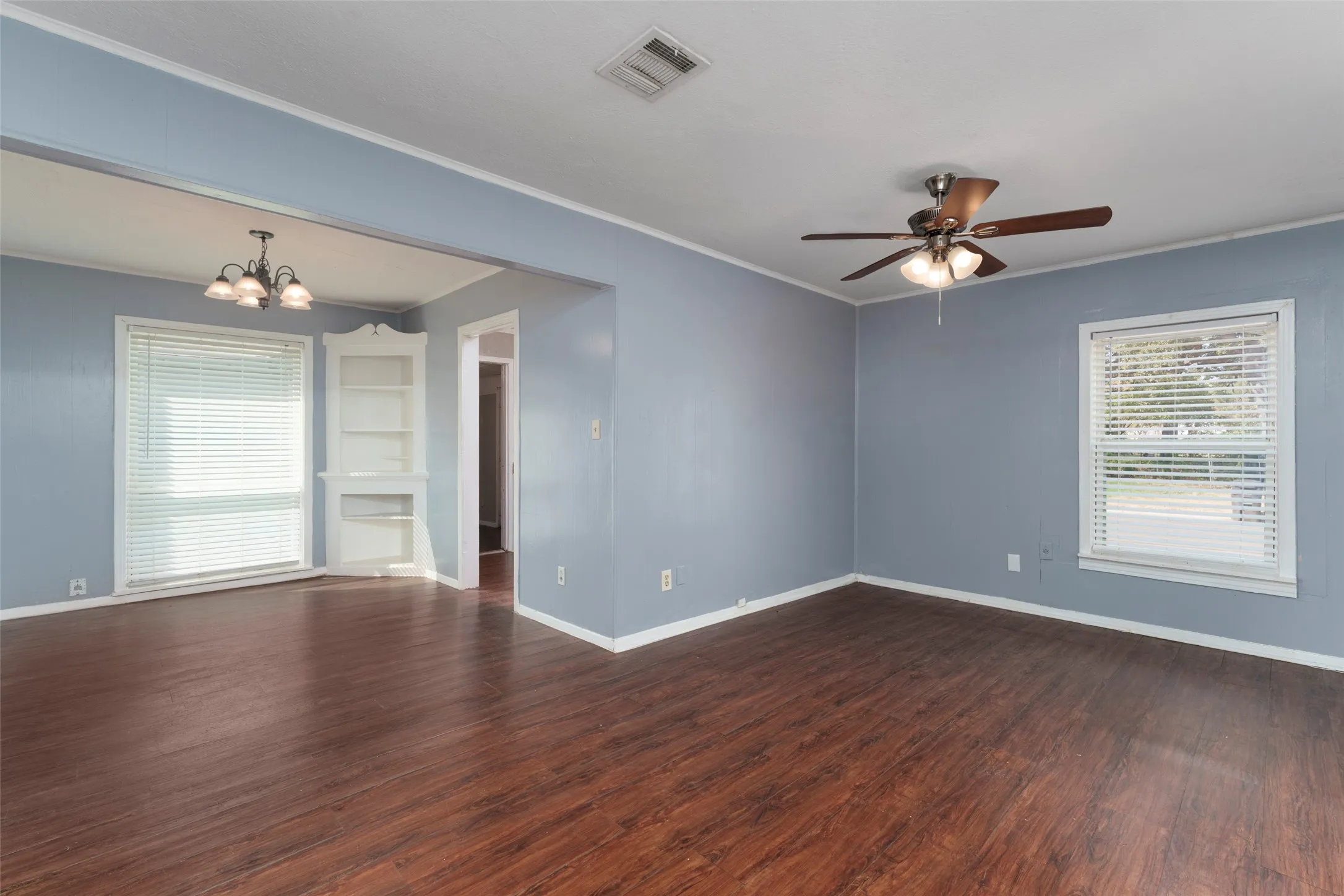 Wood-finish flooring, ceiling fan with integrated lighting, chandelier, and a built-in corner display cabinet