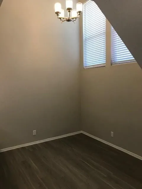 High ceilings with a five-light chandelier, dual windows with horizontal blinds, and wood-finish flooring
