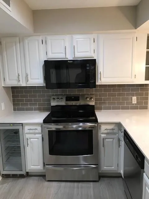 White cabinetry, stainless steel appliances, gray subway tile backsplash, light-toned wood-finish flooring, and white countertops