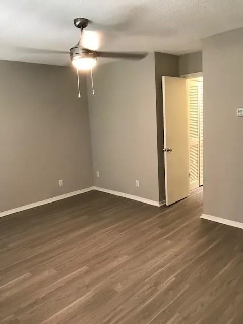 Wood-finish flooring throughout, ceiling fan with integrated lighting, neutral wall paint, and white trim