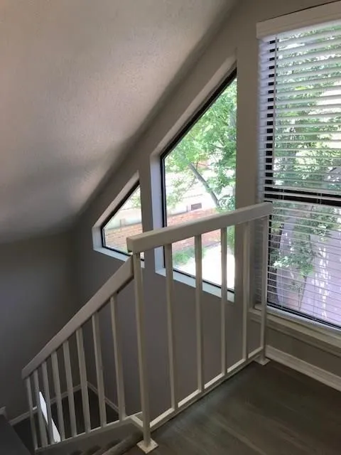 Staircase featuring wood-finish flooring, white railing, and multiple windows with blinds