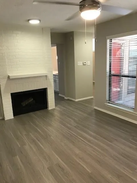 Wood-finish flooring, white brick fireplace, modern ceiling fan with integrated lighting, recessed ceiling lighting, and window with blinds
