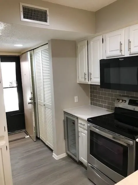 White shaker cabinetry, stainless steel appliances, gray subway tile backsplash, light wood-finish flooring, and a built-in beverage refrigerator