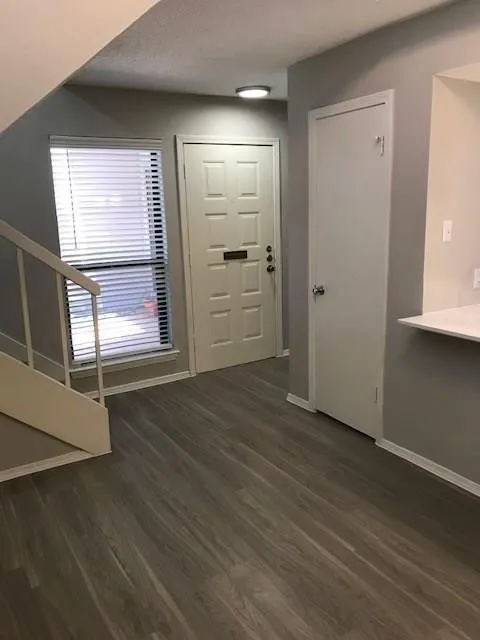Wood-finish flooring, staircase with a white railing, window with blinds, panel door, and flush-mount ceiling lighting