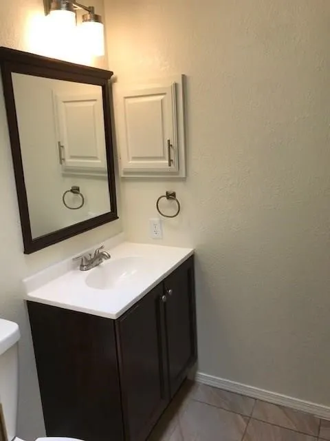 Vanity with a white countertop and integrated sink, dark wood-finish cabinetry, and a framed mirror
