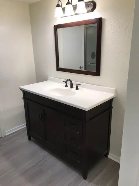 Dark wood-finish vanity with white countertop and integrated sink, framed mirror, and three-light fixture