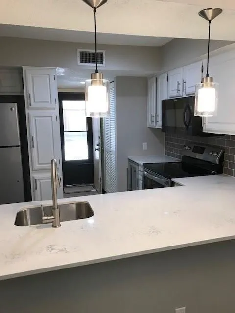 White shaker-style cabinetry, stainless steel sink with a high-arc faucet, light-toned countertops, subway tile backsplash, and pendant lighting