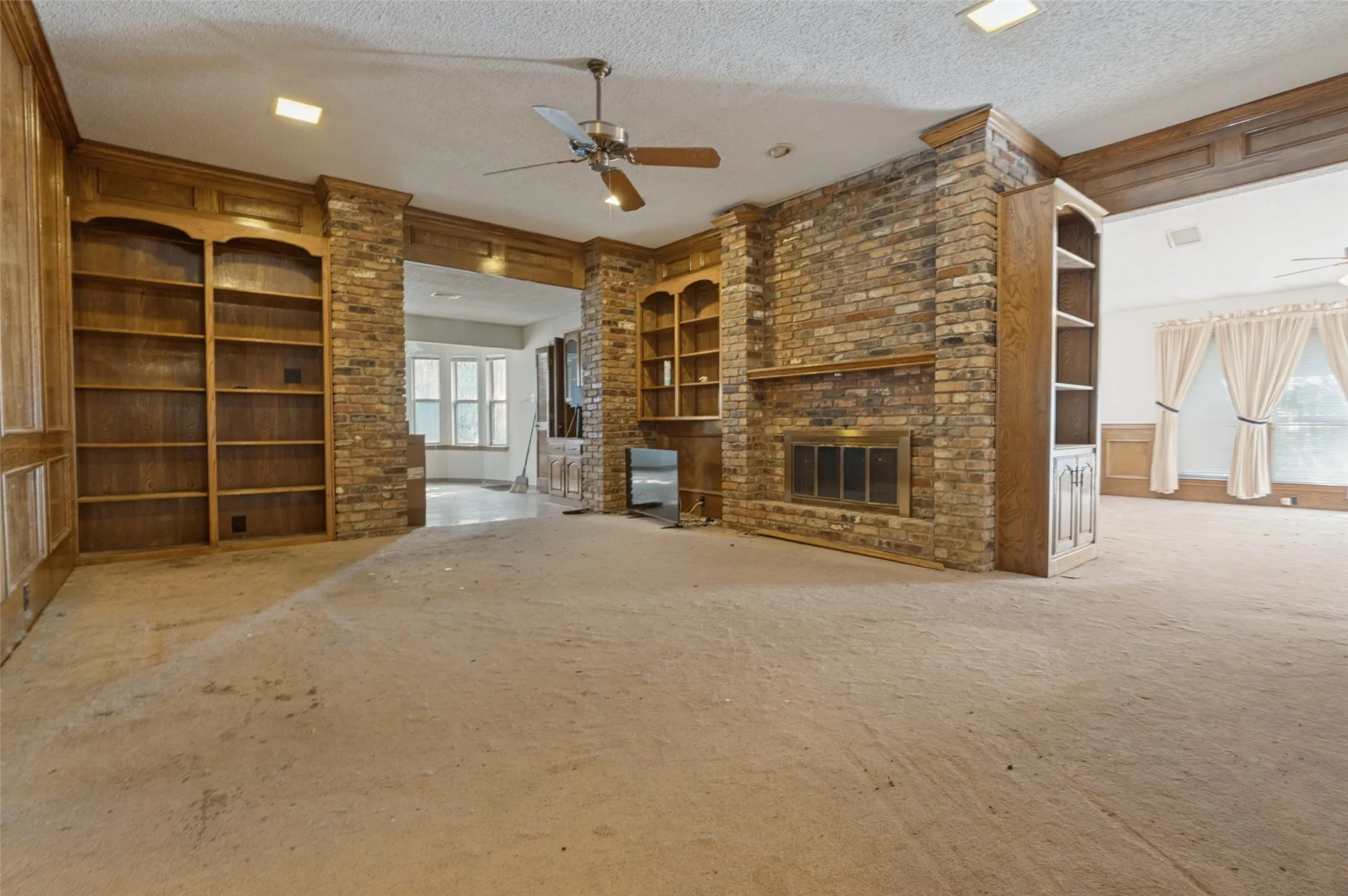 Brick-clad fireplace with metal grate, built-in wooden shelving, wooden paneling, and a ceiling fan with integrated lighting