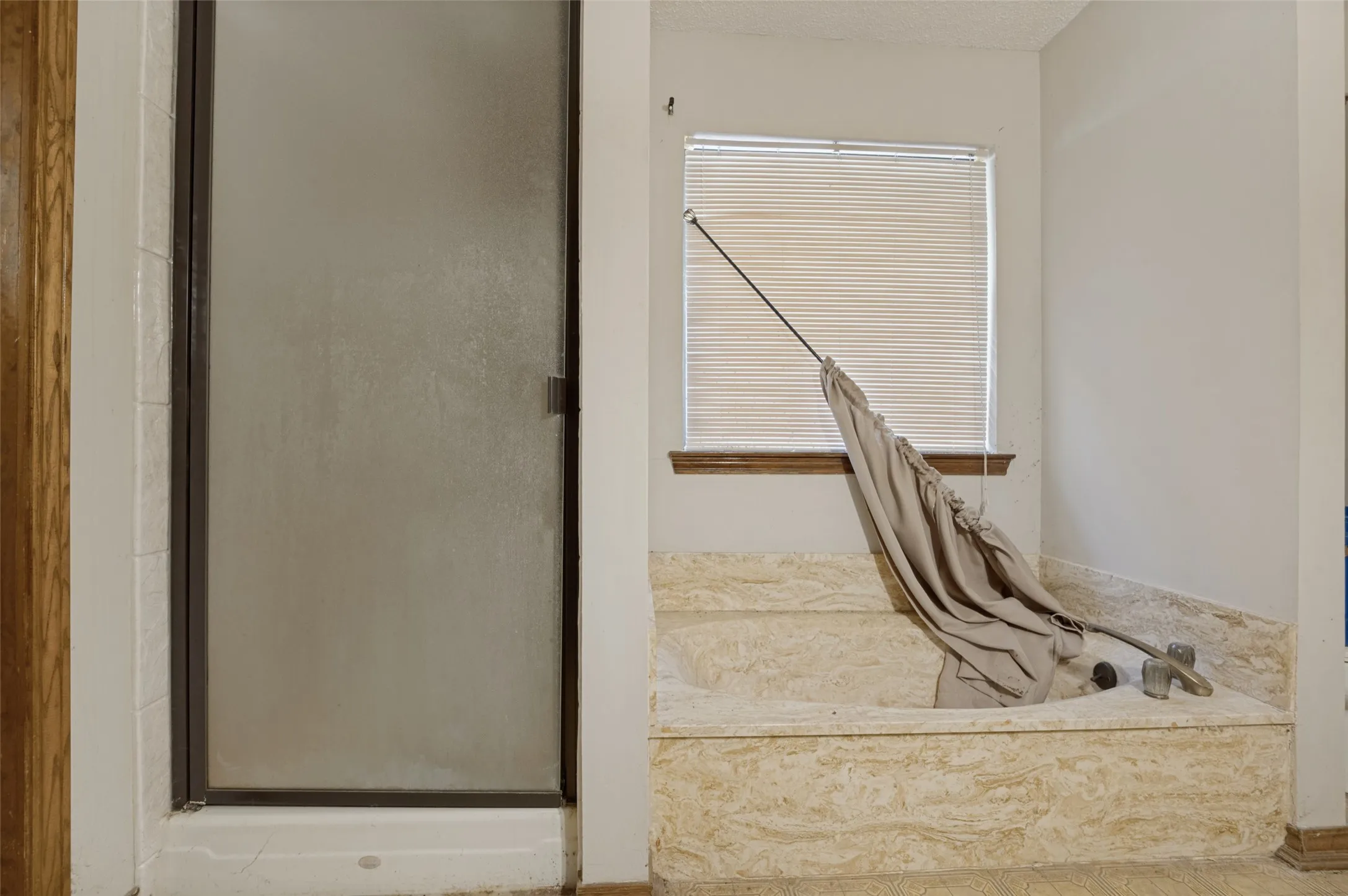 Built-in soaking tub with stone surround, a window with horizontal blinds, and a glass-enclosed shower