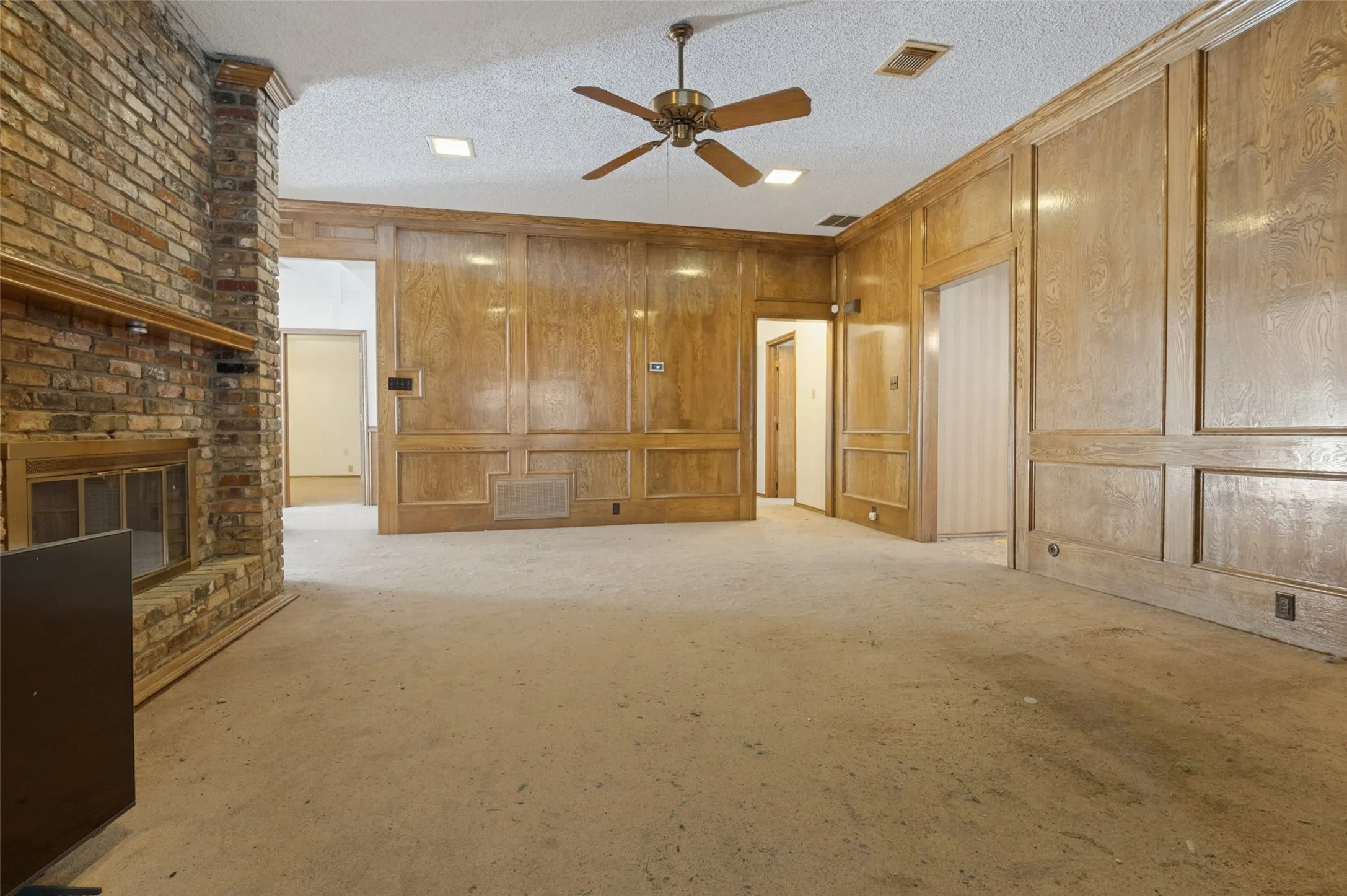 Exposed brick fireplace, wood paneling, recessed lighting, and a ceiling fan