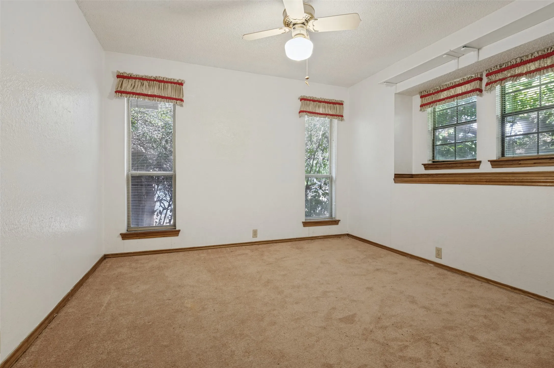 Neutral wall finish with a textured surface, multiple windows, built-in wooden trim, and a ceiling fan with integrated lighting