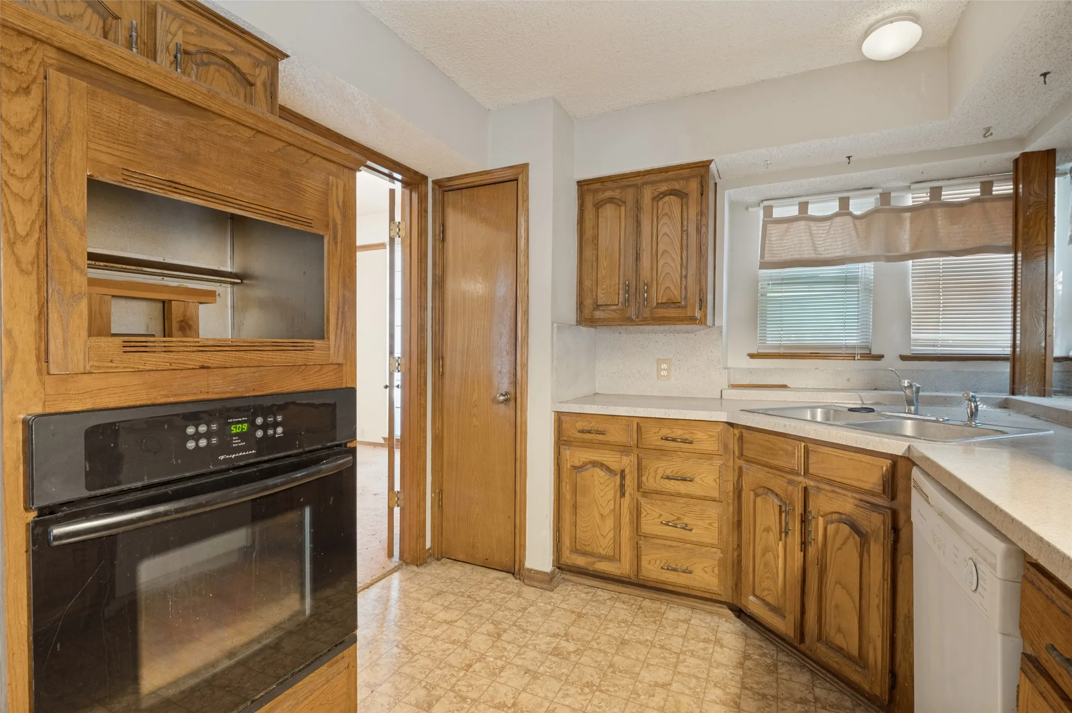 Hardwood-finish cabinetry, built-in wall oven, double basin sink, light-toned countertops, and patterned flooring
