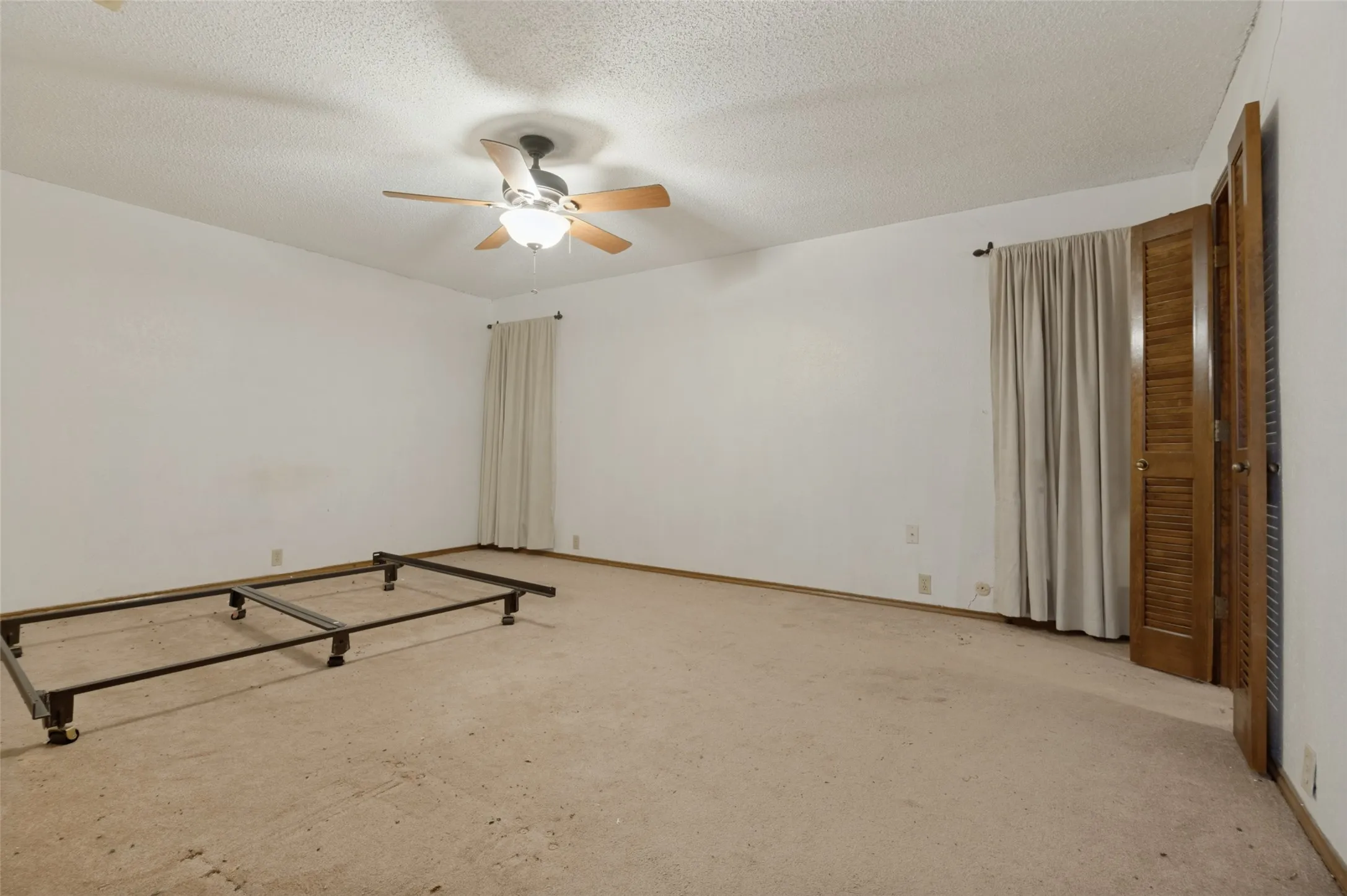 Carpeted room with white walls, a ceiling fan with light fixture, and louvered bi-fold closet doors
