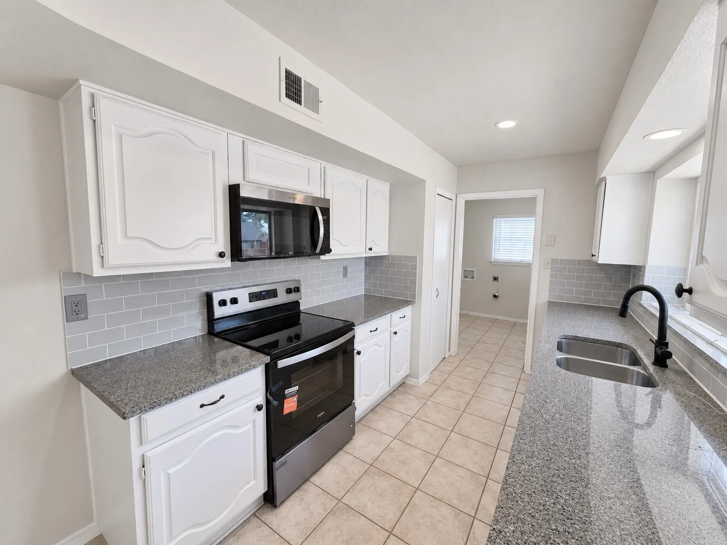 Kitchen featuring white cabinetry, gray subway tile backsplash, stainless steel appliances, and dual basin sink with a matte black faucet