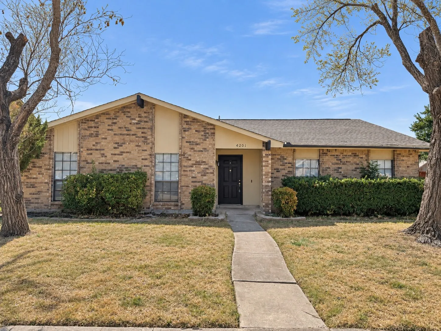Brick exterior with gabled roofline, concrete pathway, dark entry door, and established foundation plantings