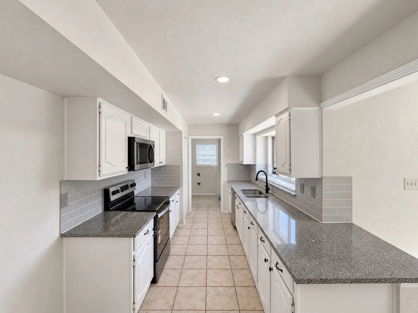 Kitchen featuring white cabinetry, gray subway tile backsplash, dark-toned countertops, tile flooring, and a stainless steel sink with a matte black faucet