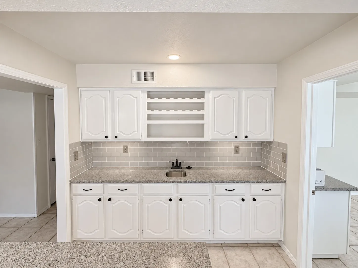White cabinetry with black hardware, integrated wine rack, undermount sink with a black faucet, gray subway tile backsplash, and speckled countertops