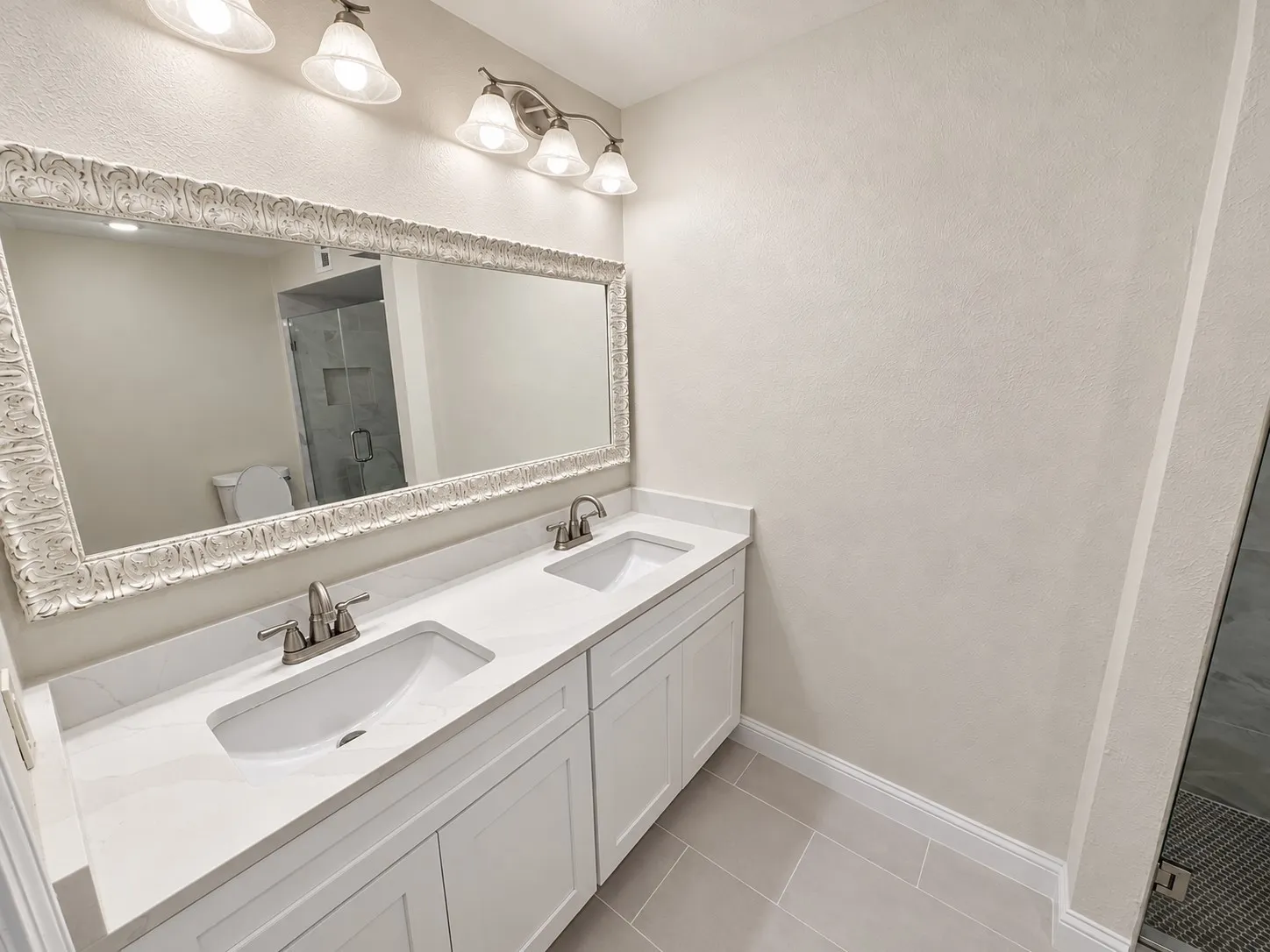 Dual vanity with white shaker-style cabinetry, white countertops, undermount sinks, and brushed nickel hardware