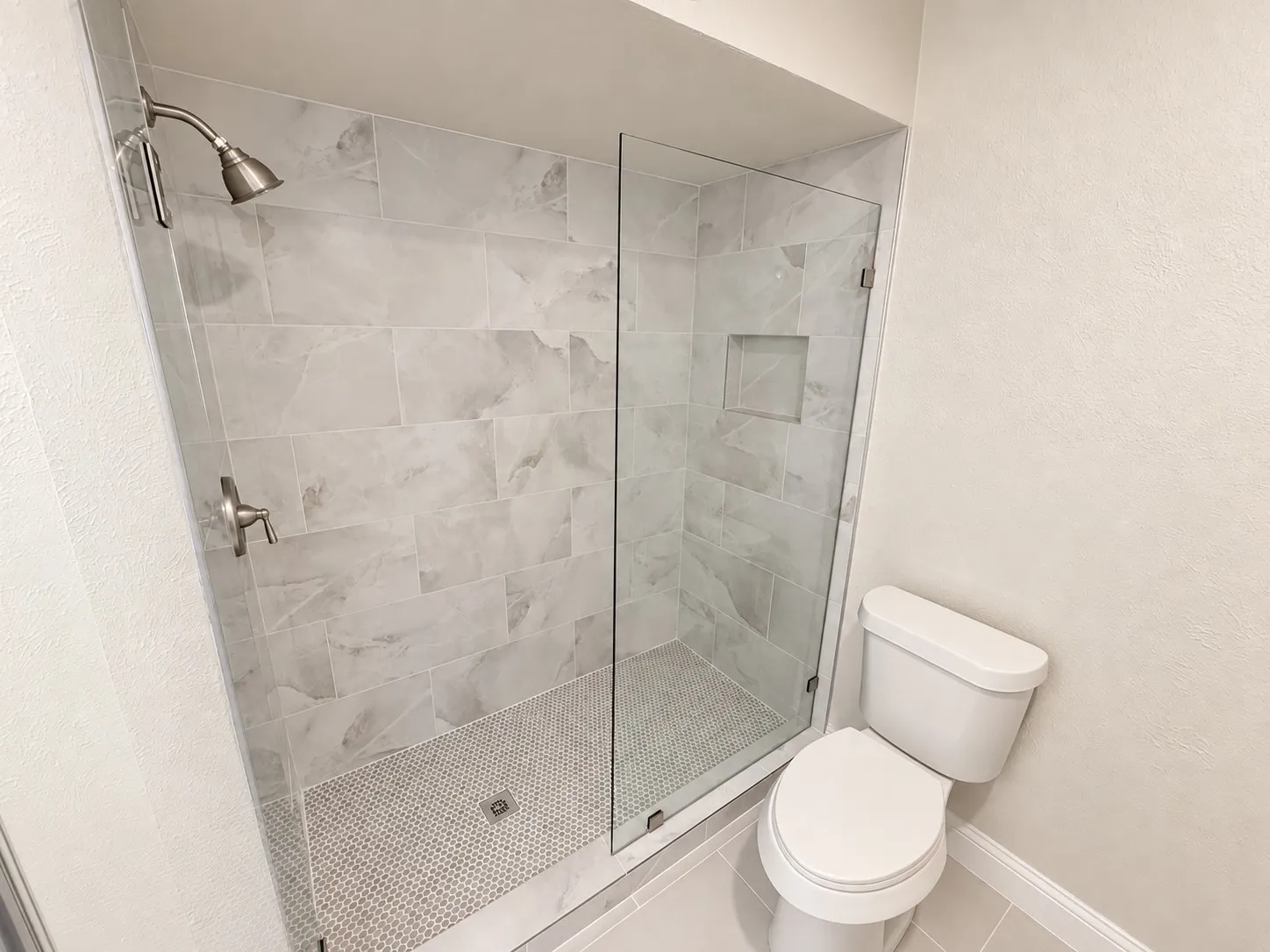 Glass-enclosed shower with brushed nickel fixtures, tiled walls, and a built-in shower niche