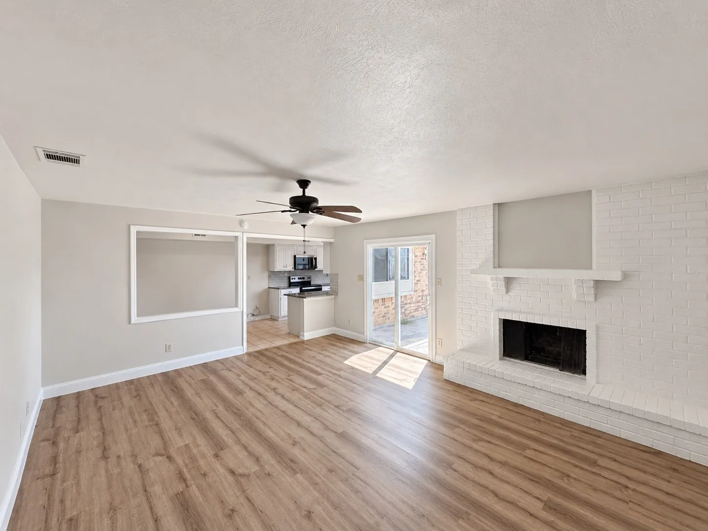 Wood-finish flooring, white brick fireplace with mantel, ceiling fan, and sliding glass door