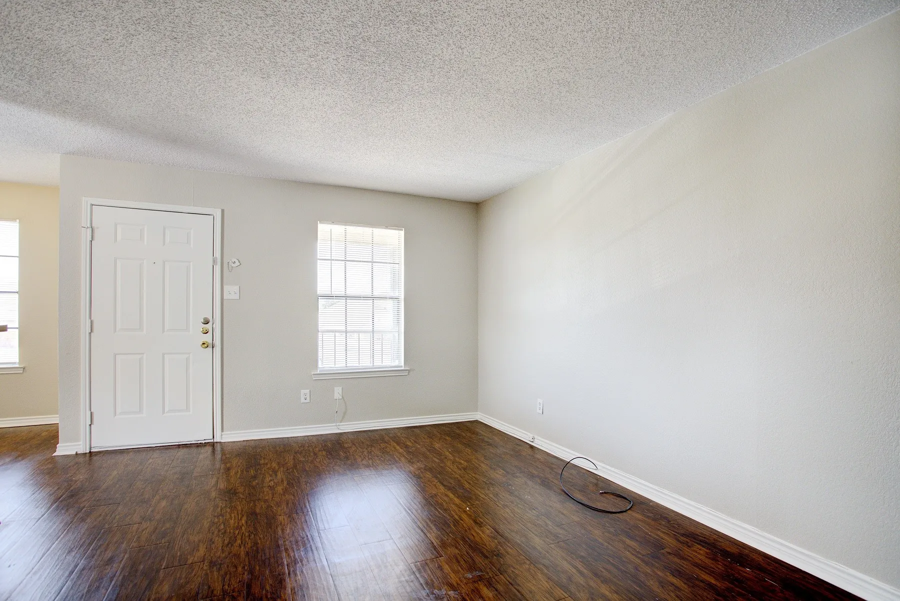 Wood-finish flooring, white paneled entry door, multiple windows with grilles, and light-toned wall finishes