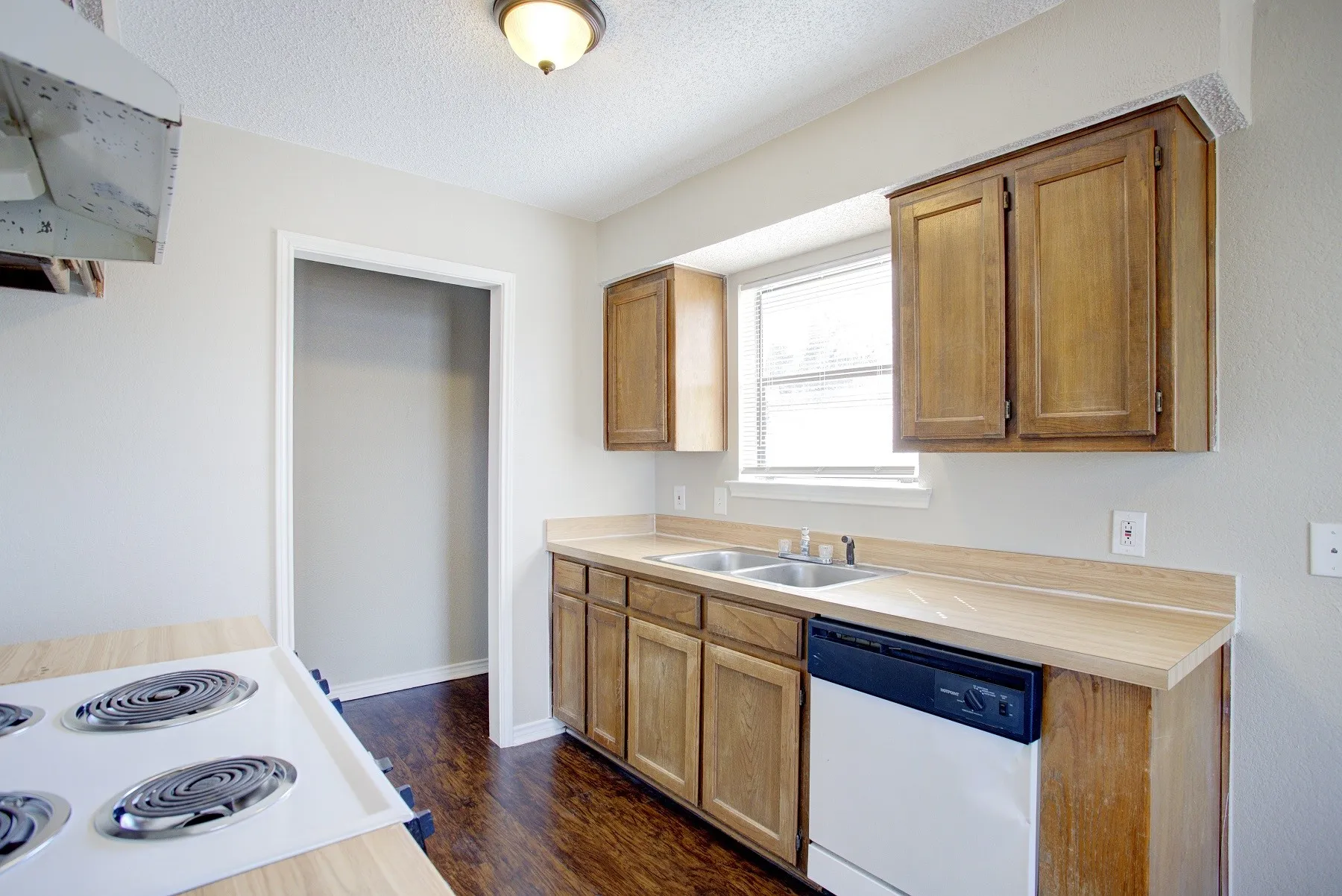 Kitchen featuring wood-finish cabinetry, a double basin sink, a built-in dishwasher, and wood-finish flooring