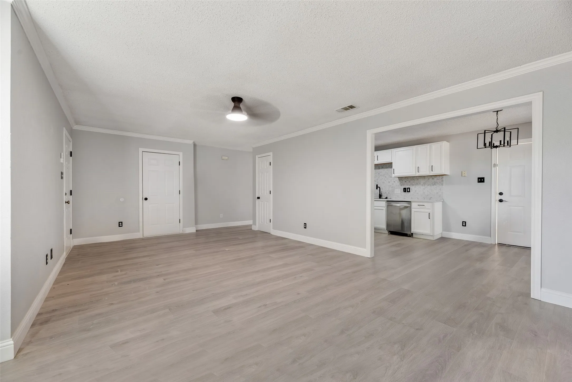 Open-concept living area featuring wood-finish flooring, crown molding, and a modern ceiling fixture