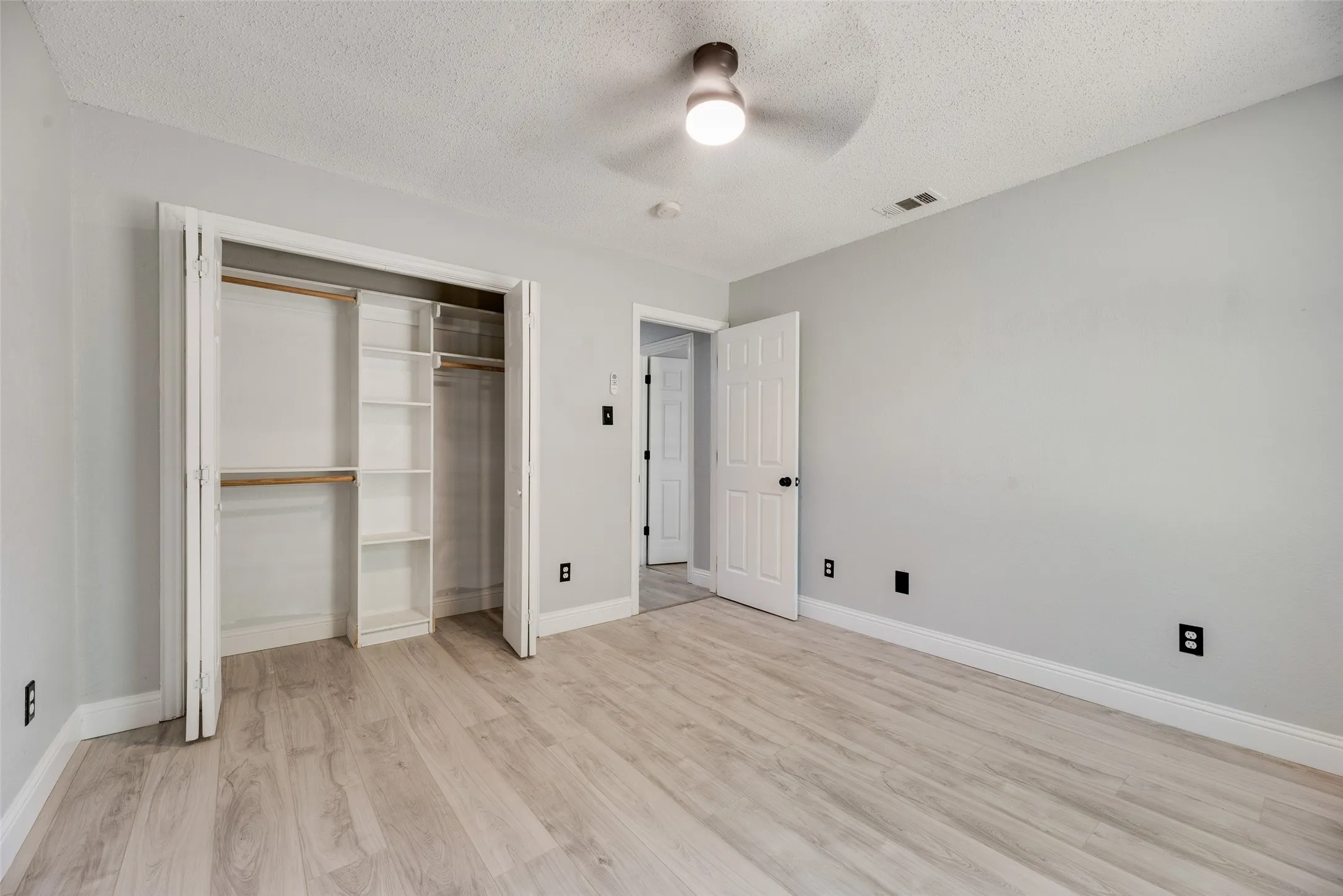 Wood-finish flooring, light gray wall paint, and a ceiling fan with integrated lighting