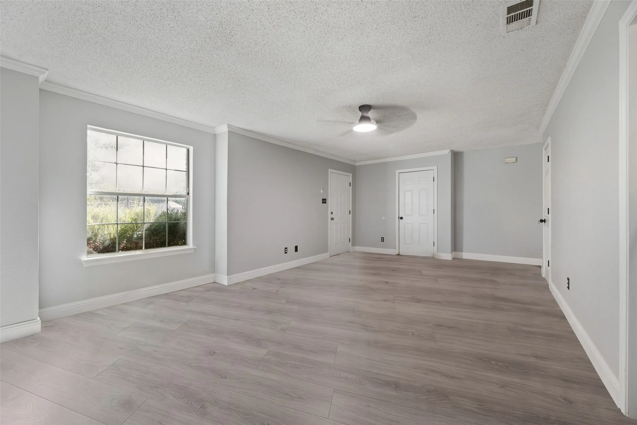 Spacious room featuring light gray walls, white trim, wood-finish flooring, a ceiling fan, and a large window