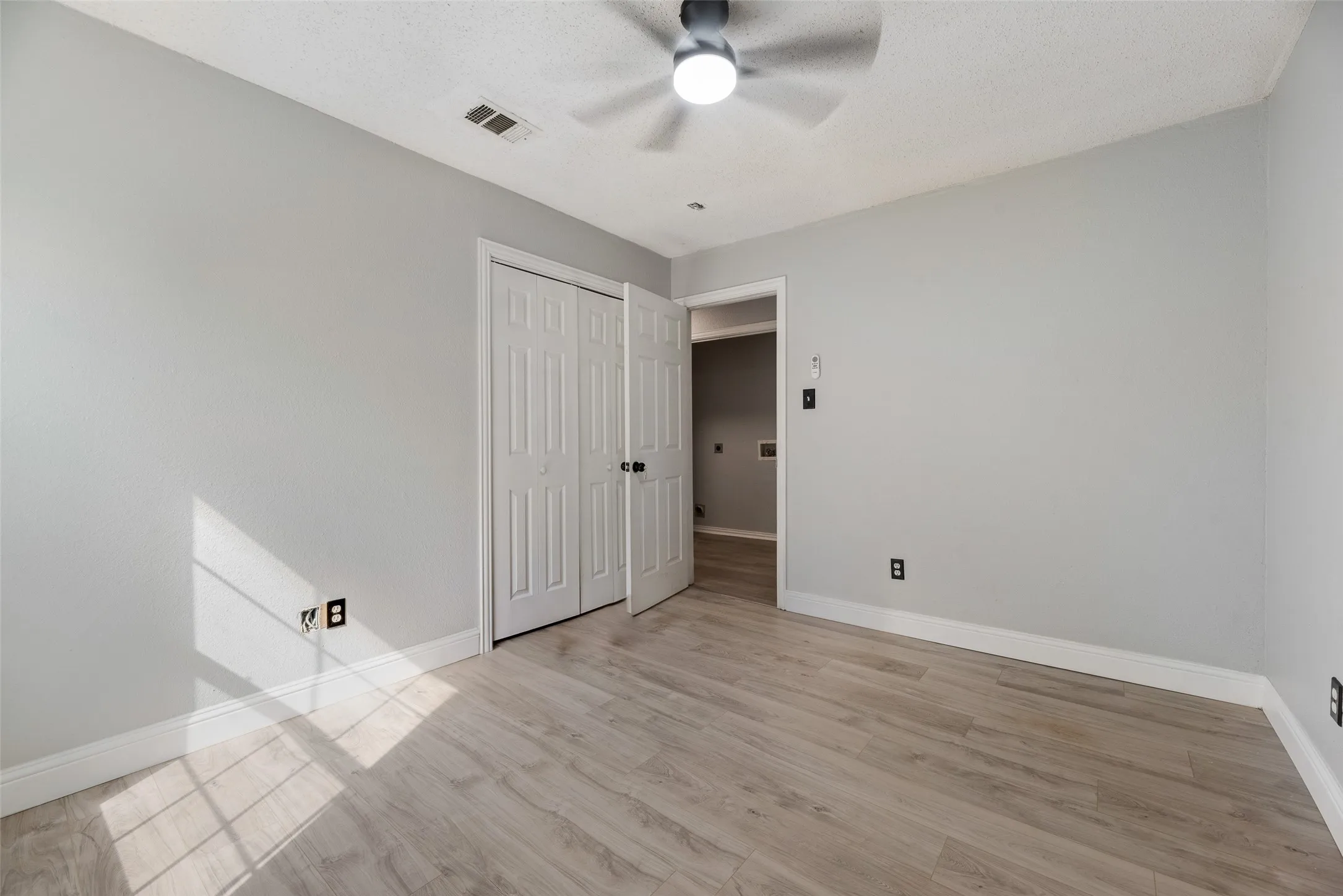 Wood-finish flooring, ceiling fan with integrated lighting, bi-fold closet doors, and light gray wall paint