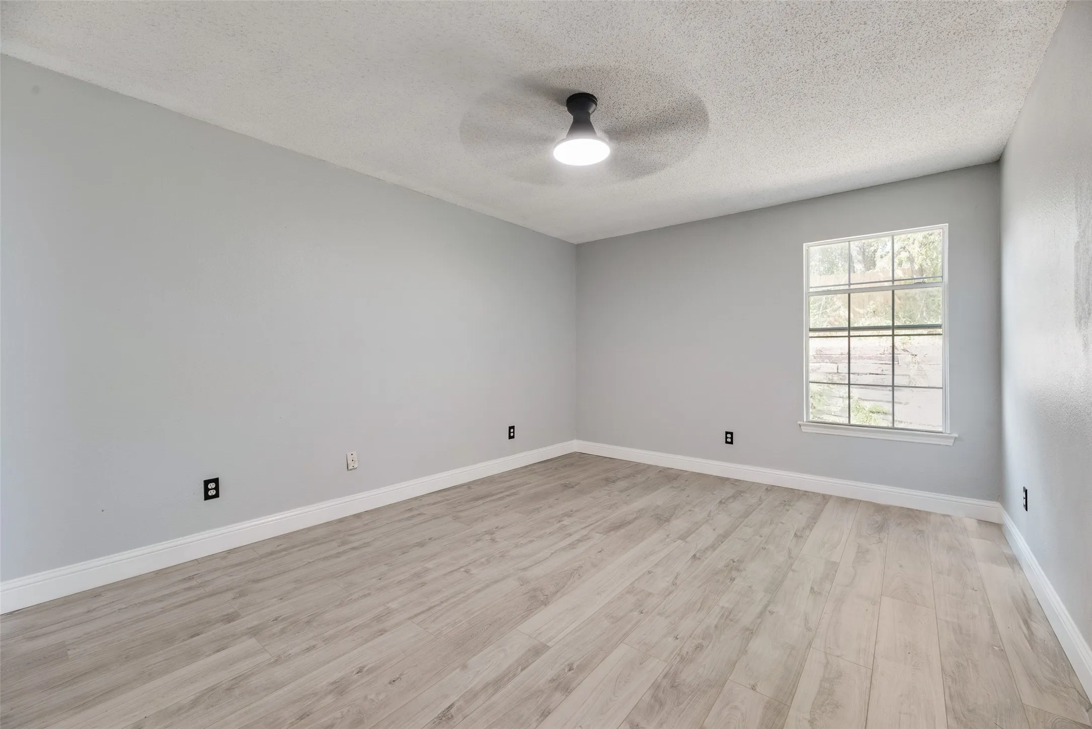 Wood-finish flooring with white trim, light gray walls, and a ceiling fan with integrated lighting
