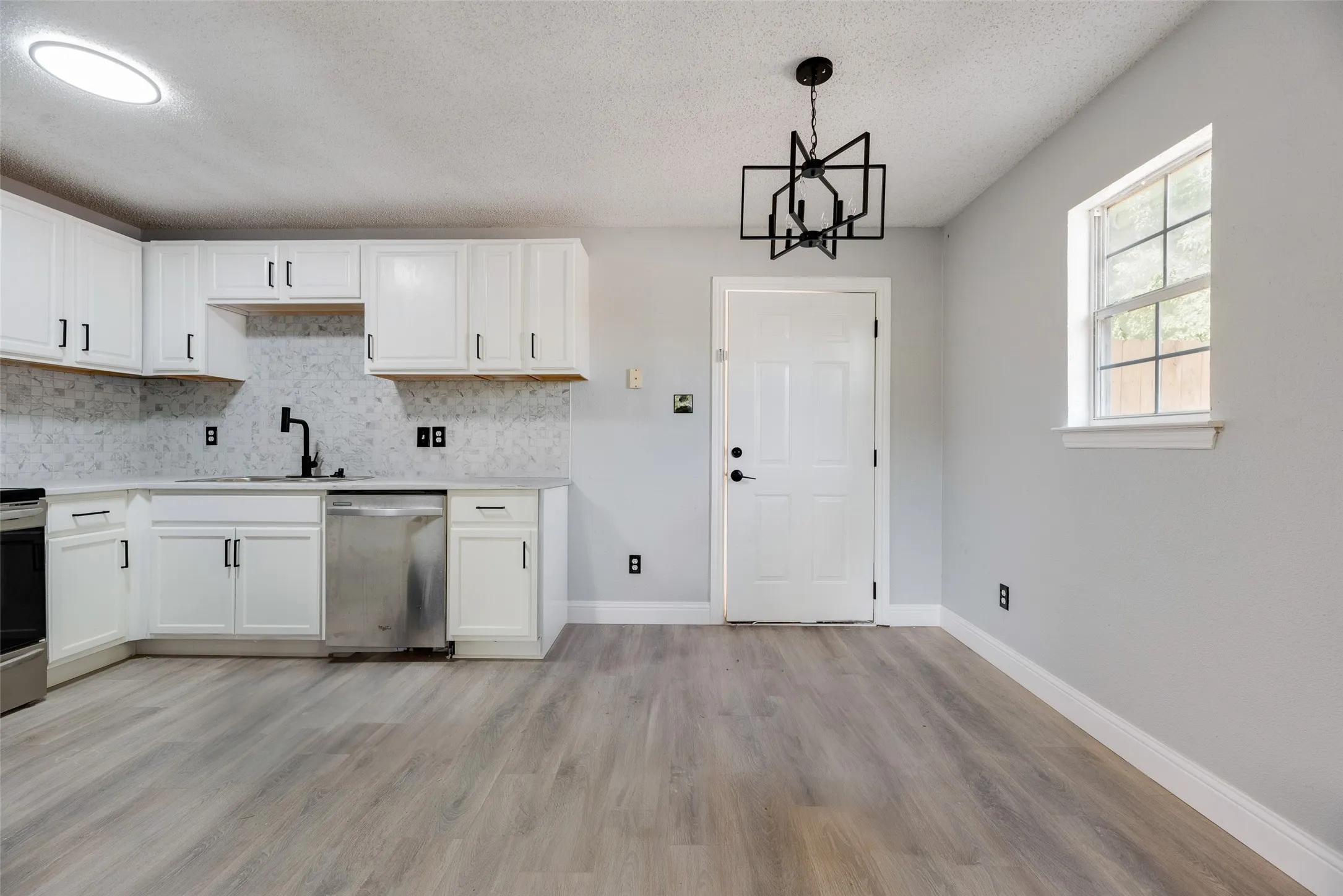 Kitchen featuring white cabinetry, light-toned countertops, a full tile backsplash, stainless steel appliances, and wood-finish flooring