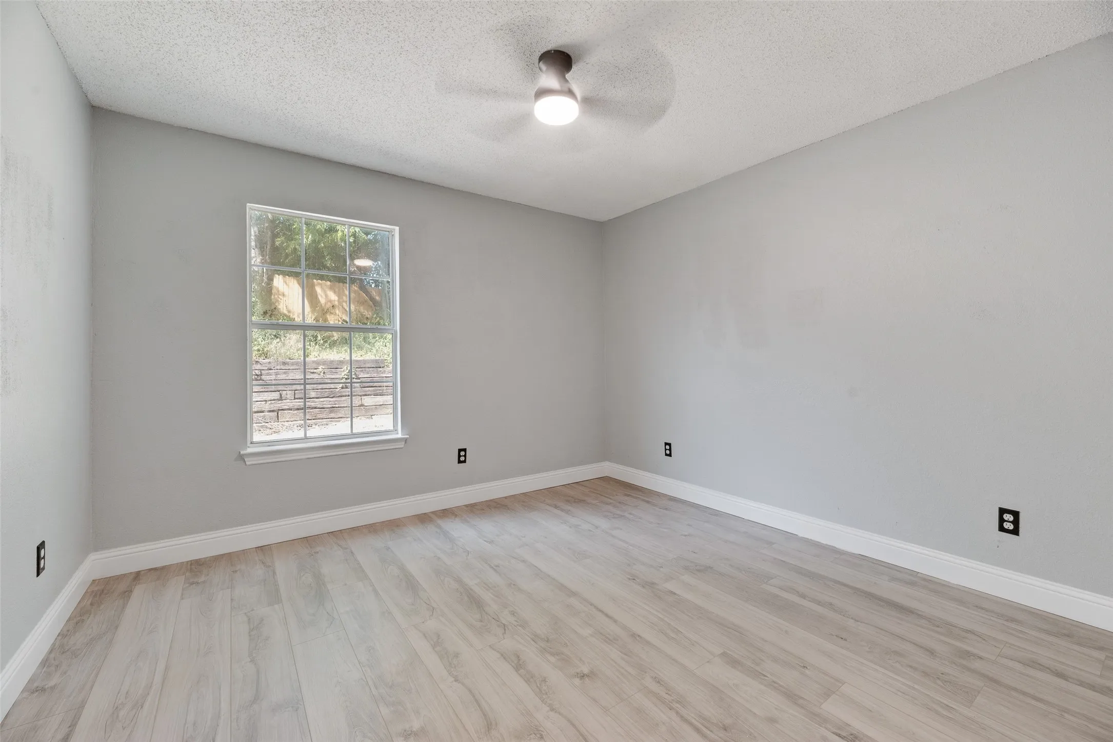 Light gray painted walls with white trim, wood-finish flooring, and a ceiling fan with integrated lighting